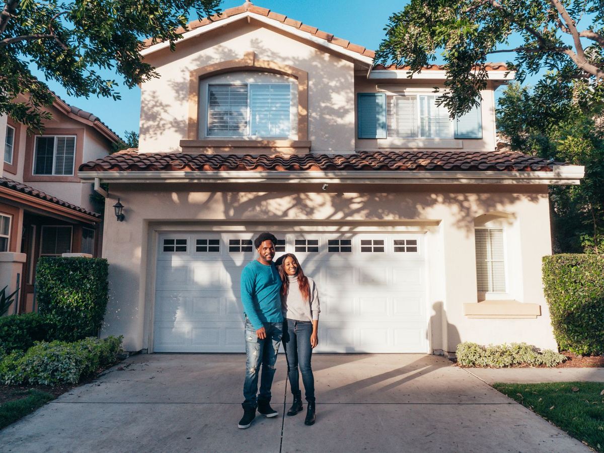 Smiling couple standing in the driveway of their two-story home